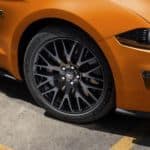 A closeup is shown of the wheel on an orange 2020 Ford Mustang in a parking lot.