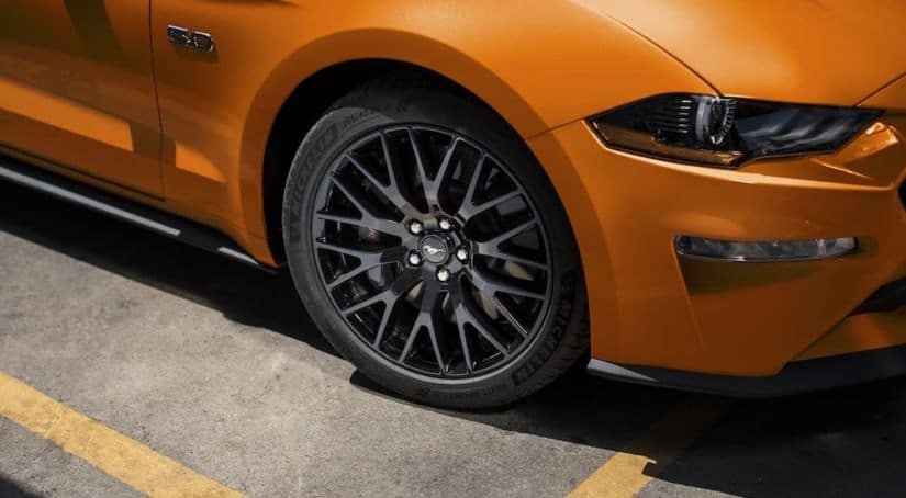 A closeup is shown of the wheel on an orange 2020 Ford Mustang in a parking lot.