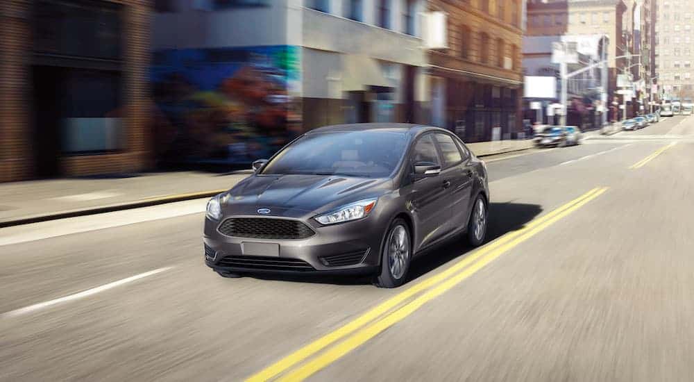A grey 2016 Ford Certified Pre-Owned Focus is driving on a city street.