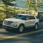 A white 2017 Ford Explorer is driving on a winding road through trees.