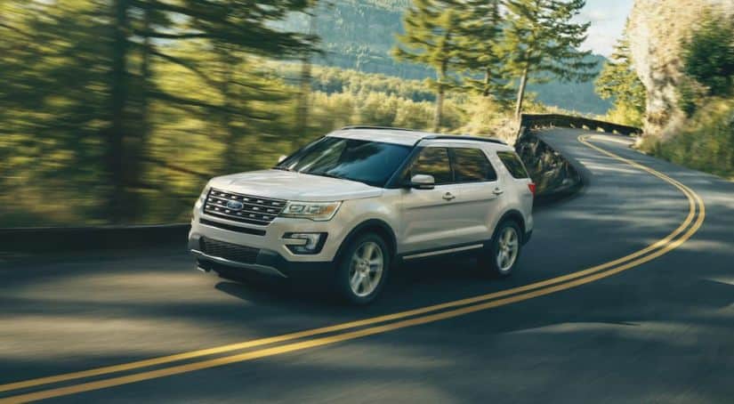 A white 2017 Ford Explorer is driving on a winding road through trees.