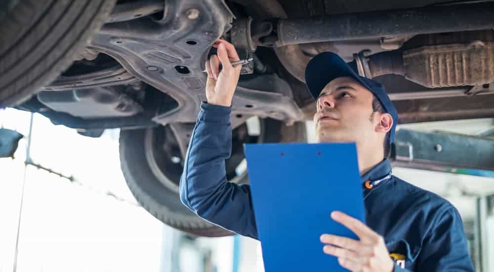 A mechanic is underneath a Ford Certified Pre-Owned vehicle with a blue clipboard.