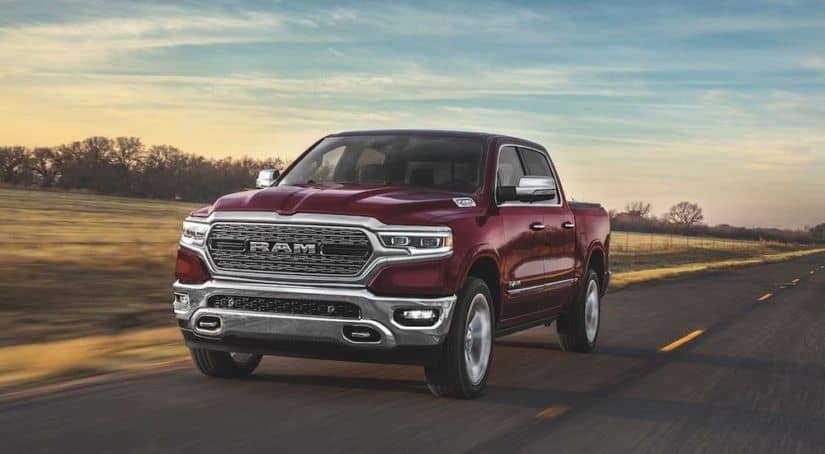 A dark red 2020 Ram 1500 from a Ram dealer near me is driving along a highway at dusk.