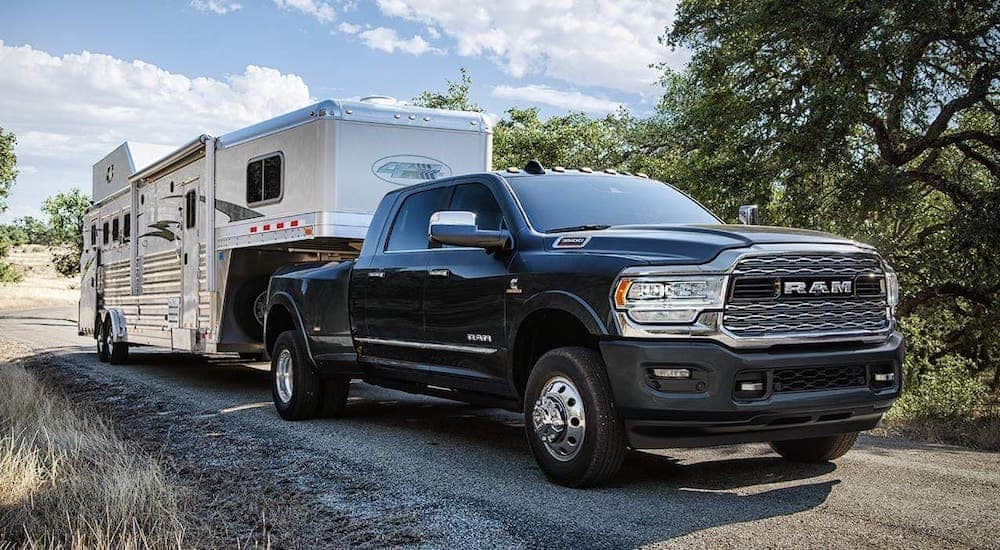 A black 2020 Ram 3500 is towing a large camper on a gravel road.