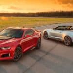 A red and a silver 2018 Chevy Camaro are parked on a race track at sunset.