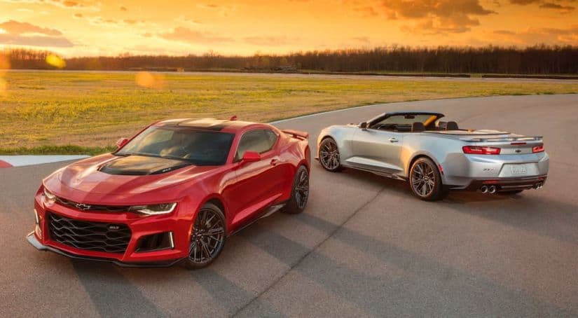 A red and a silver 2018 Chevy Camaro are parked on a race track at sunset.