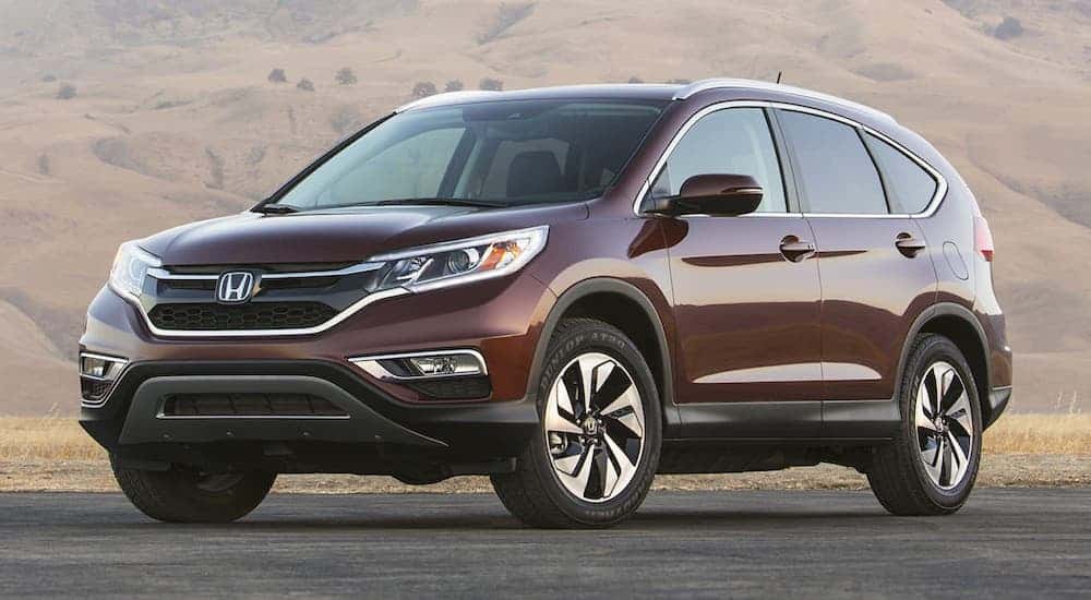 One of the popular used SUVs for sale, a red 2015 Honda CR-V, is parked in front of a mountain.
