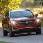 A red 2020 Buick Enclave Sport Touring is driving on a tree-lined road.