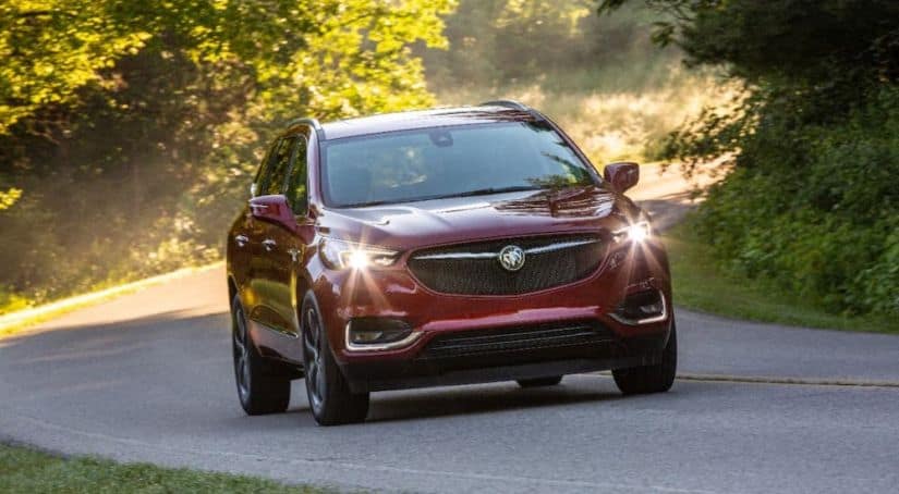 A red 2020 Buick Enclave Sport Touring is driving on a tree-lined road.