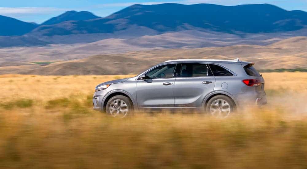 A silver 2020 Kia Sorento is driving in a field with mountains in the distance.