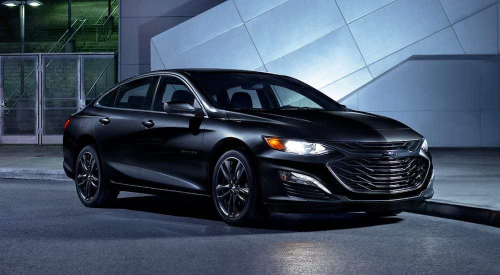 An all black 2020 Chevy Malibu is parked outside a lit up building at night.