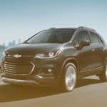 A dark grey 2020 Chevy Trax is driving away from a city skyline.