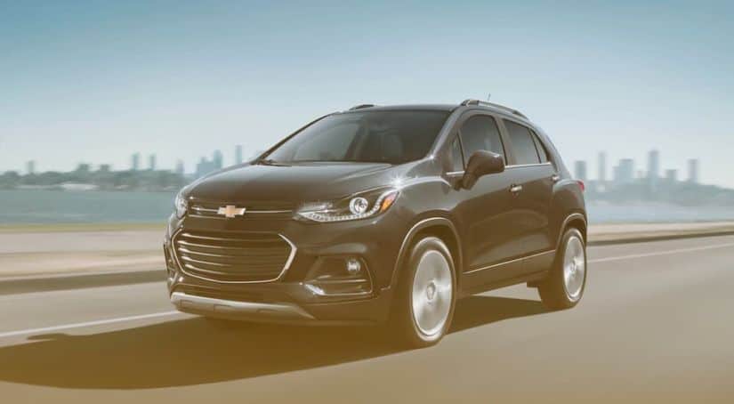 A dark grey 2020 Chevy Trax is driving away from a city skyline.