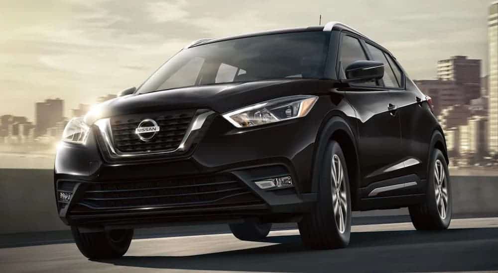A black 2020 Nissan Kicks is driving away from a city skyline.