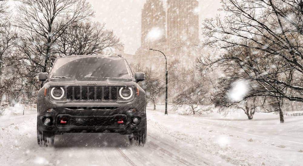 A gray 2020 Jeep Renegade Trailhawk is shown from the front on a snowy road in front of a city.