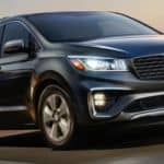 A black 2020 Kia Sedona is driving on a highway past a blurred town.