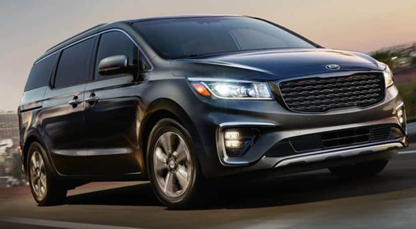 A black 2020 Kia Sedona is driving on a highway past a blurred town.