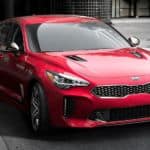 A red 2020 Kia Stinger is driving on a city street.