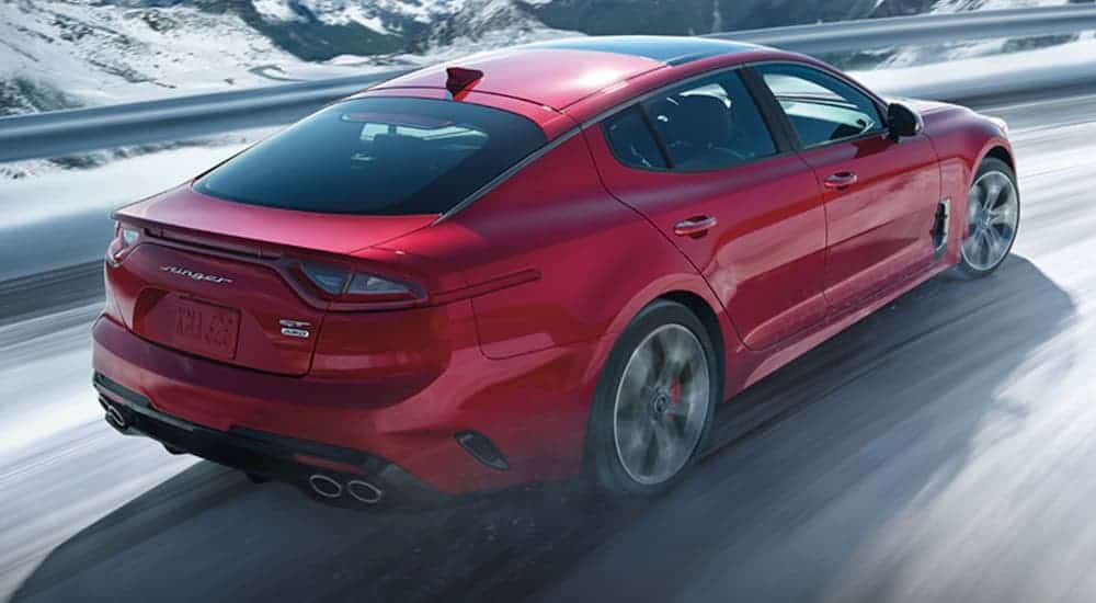 A red 2020 Kia Stinger is driving quickly on a snow covered road.