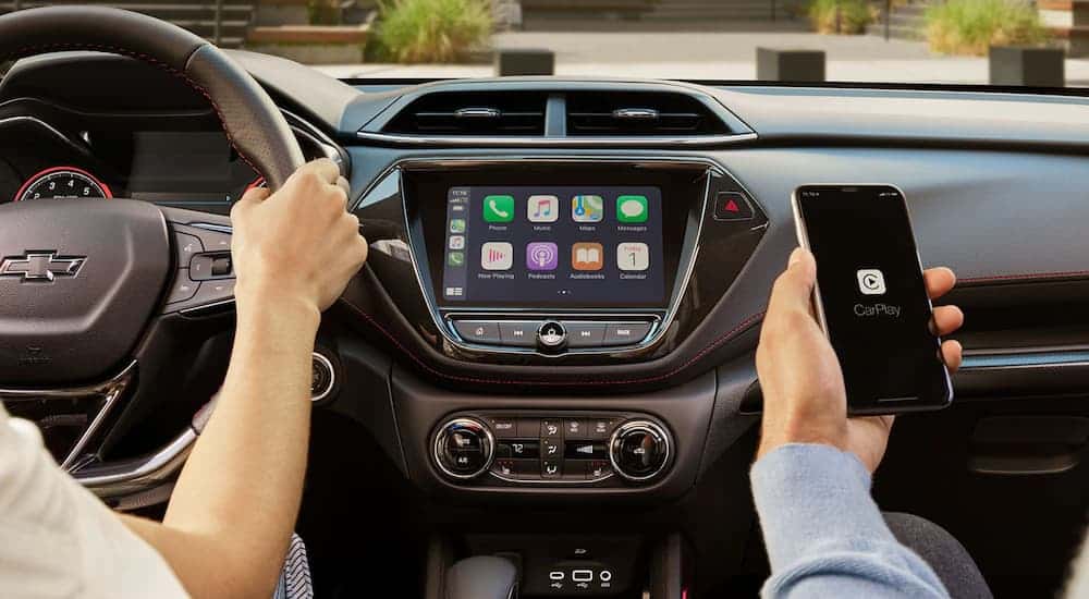 A passenger is using the Apple CarPlay feature on their phone in front of the infotainment screen in a 2021 Chevy Trailblazer.