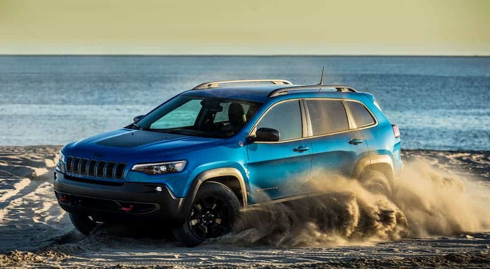 A blue 2020 Jeep Cherokee is driving in the sand at a beach.