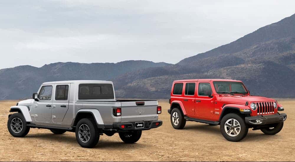A red 2020 Jeep Wrangler Unlimited is parked next to a silver 2020 Jeep Gladiator on dirt in front of a mountain.