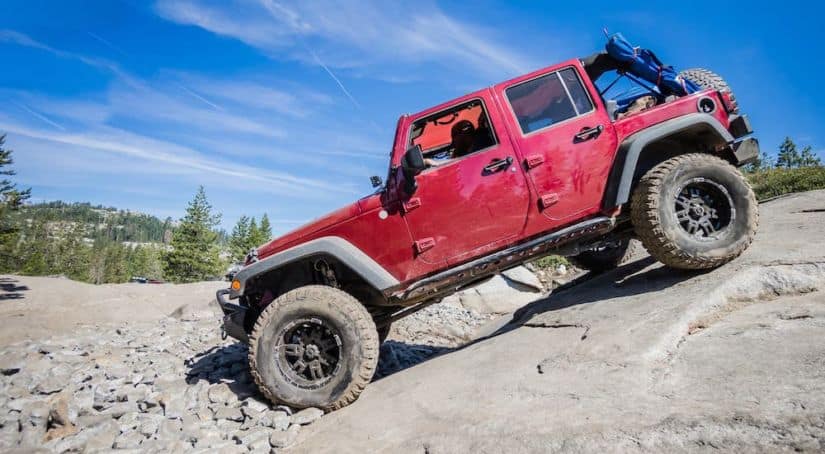 A red Jeep Wrangler Unlimited is climbing down a rock against a blue sky.