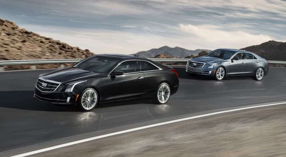 A grey 2017 used Cadillac ATS is following a black one on a road with distant hills.