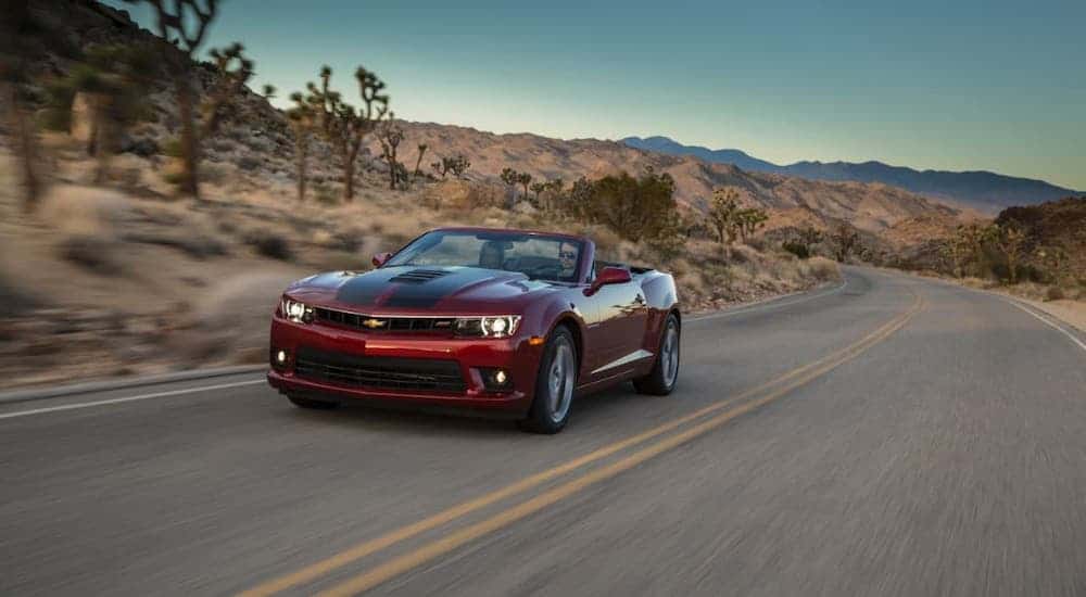 A red convertible 2015 Chevy Camaro SS is driving on a desert road.