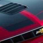 A closeup is shown of the red and black hood and grille on a 2015 Chevy Camaro SS.