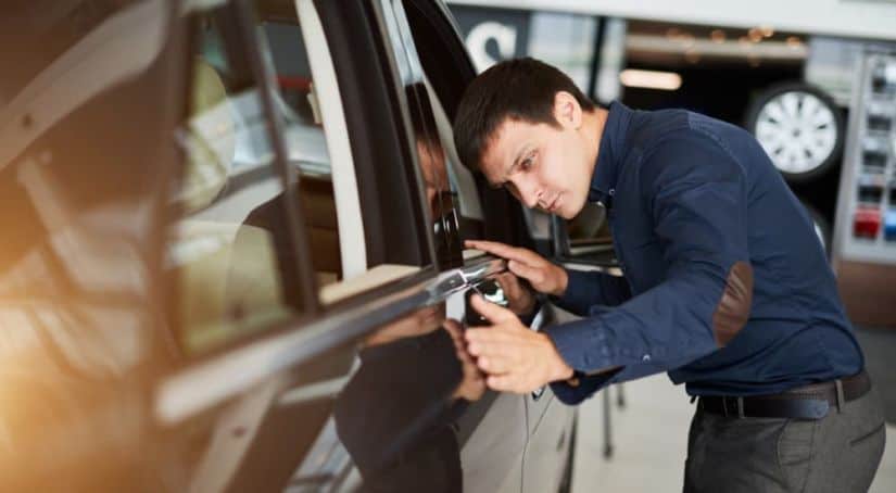 A man is looking at the exterior of a black used car.