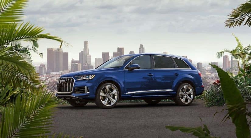 A blue 2020 Audi Q7 is parked with a city skyline in the distance.
