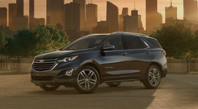 A black 2020 Chevy Equinox is in front of a city skyline at sunset after winning the 2020 Chevy Equinox vs 2020 Ford Escape comparison.