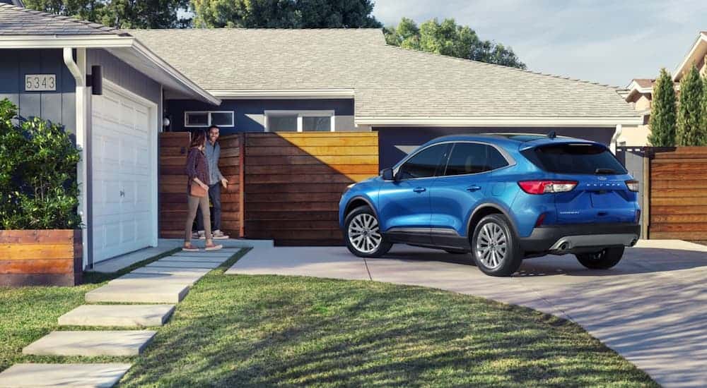 A blue 2020 Ford Escape is parked in the driveway of a blue house with a wooden fence. 