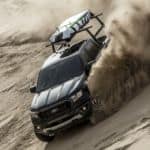 A black 2020 Ford Ranger is driving down a sand dune with a surf board on top after winning the 2020 Ford Ranger vs 2020 Chevy Colorado comparison.