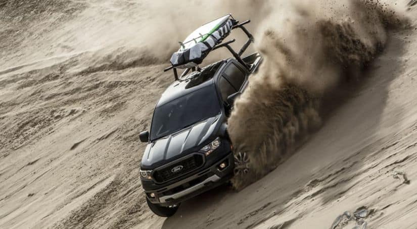 A black 2020 Ford Ranger is driving down a sand dune with a surf board on top after winning the 2020 Ford Ranger vs 2020 Chevy Colorado comparison.