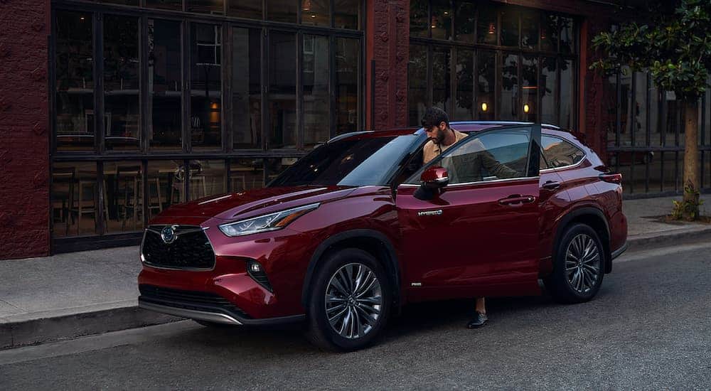 A man is getting into a burgundy 2020 Toyota Highlander parked on a city street.