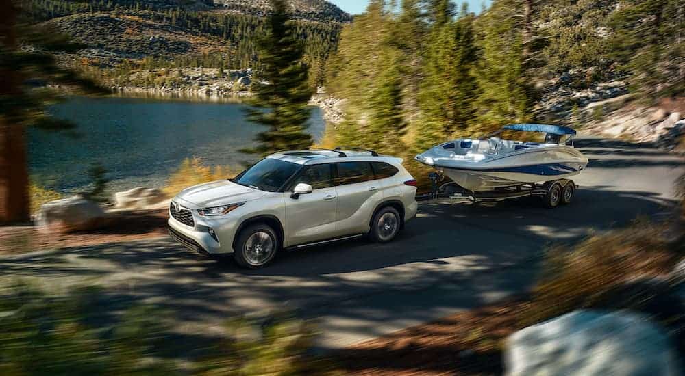 A white 2020 Toyota Highlander is towing a boat past a lake and mountain.