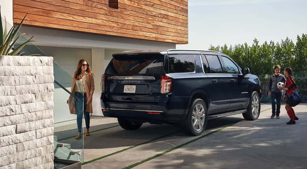 A family is next to a dark blue 2021 Chevy Suburban at a modern home.
