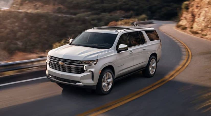 A white 2021 Chevy Suburban is driving on a winding mountain road.