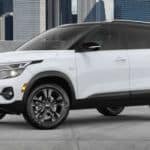 A white 2021 Kia Seltos is parked in front of city buildings for the 2021 Kia Seltos vs 2020 Kia Sportage comparison.