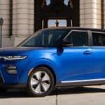 A blue 2021 Kia Soul EV is parked in front of a tan building.