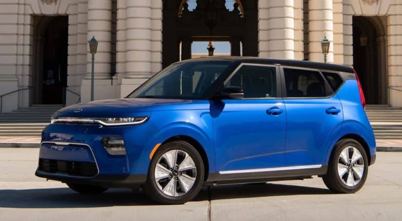 A blue 2021 Kia Soul EV is parked in front of a tan building.