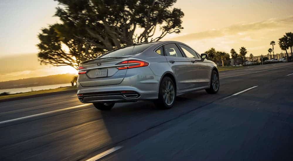 A silver 2017 Ford Fusion is driving at sunset.