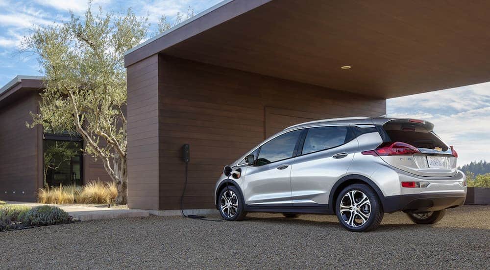 A silver 2020 Chevy Bolt EV is being charged at a modern home.