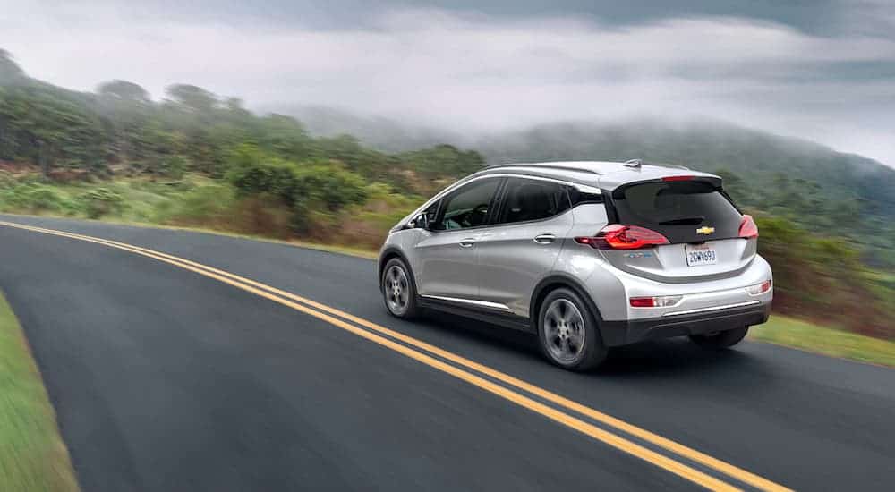 A silver 2020 Chevy Bolt EV is driving on a road with foggy views of hills after leaving a Chevy dealership.