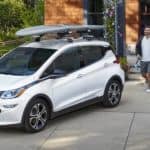 A couple is walking toward a white 2020 Chevy Bolt EV outside a modern house.