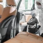 A worker is in a sanitary suit spraying the interior of a car for COVID-19.