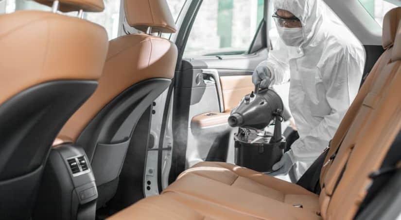 A worker is in a sanitary suit spraying the interior of a car for COVID-19.