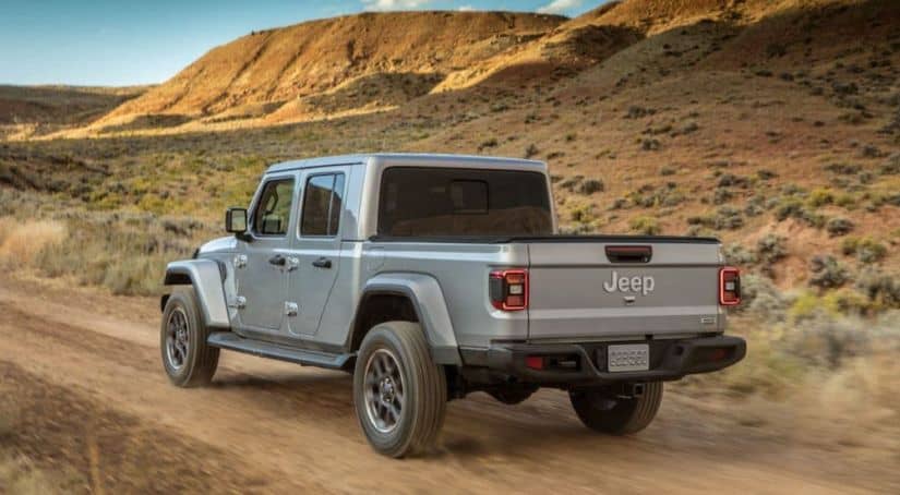 A silver 2020 Jeep Gladiator from a Jeep dealership near me is driving on a dirt road.
